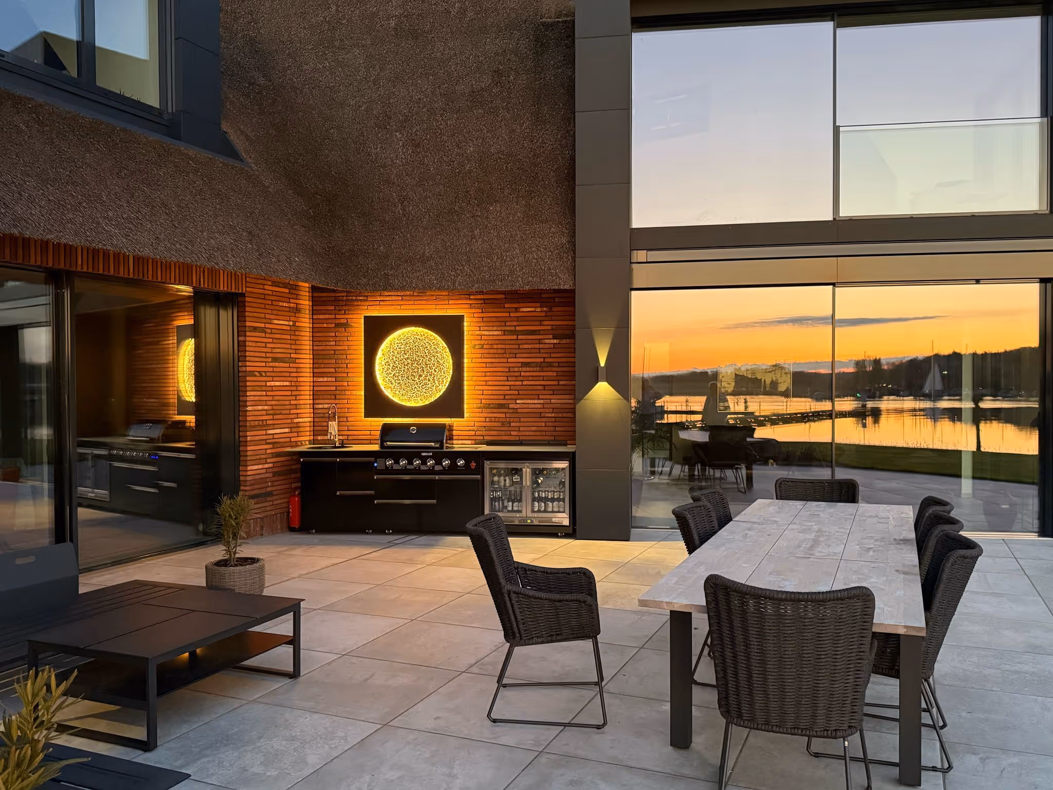 Beleuchteter Sonnenmond an einer Klinkerwand auf einer Terrasse am See bei Sonnenuntergang