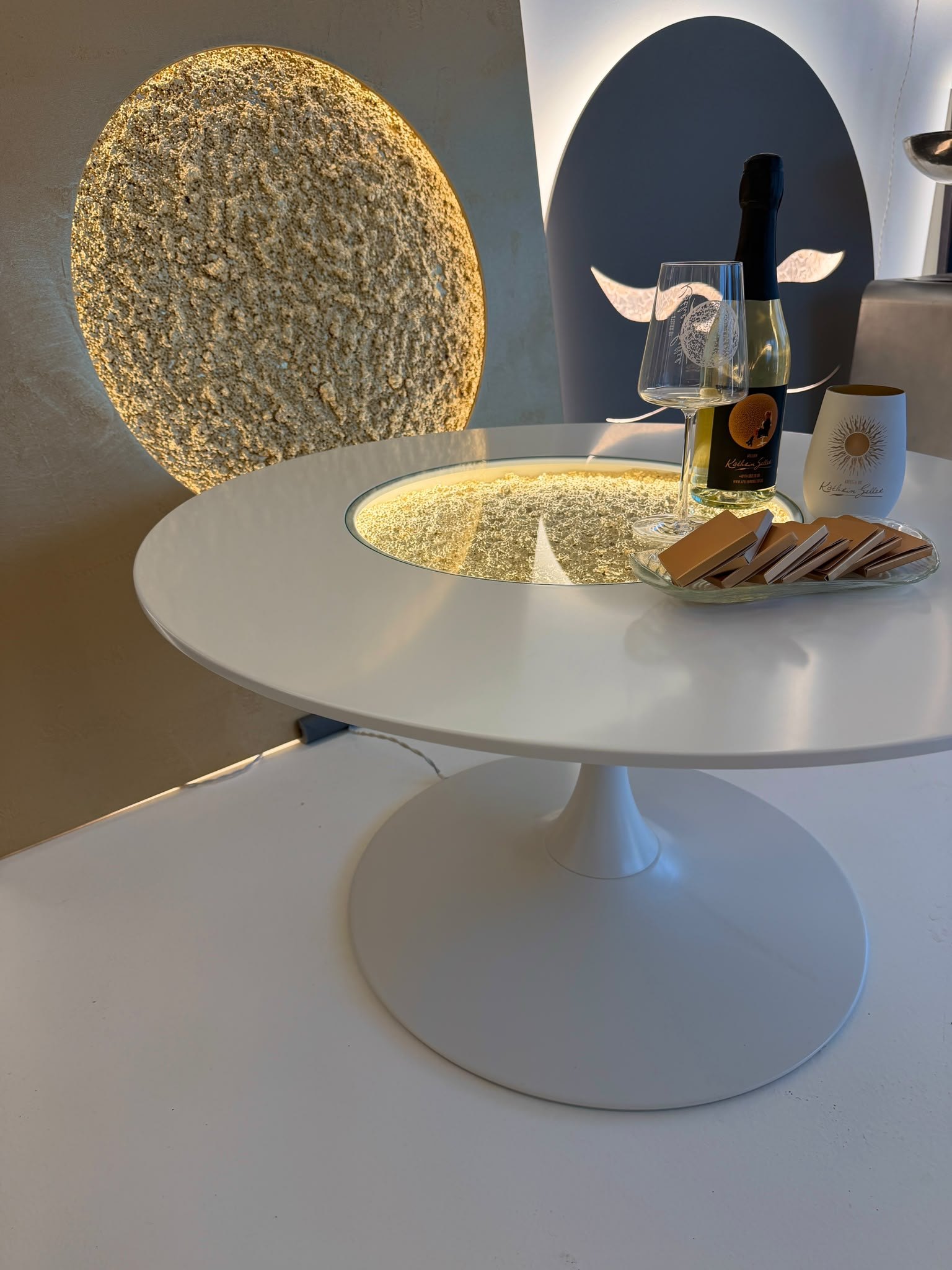 Megamond Ess-/Bürotisch in Perlmuttweiß mit goldenem Mond, Flasche und Gläser auf der Platte
