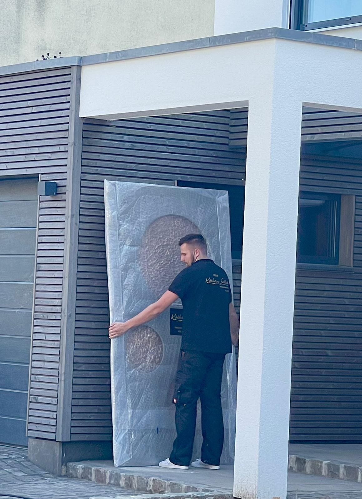 Lieferung: ein Mitarbeiter des Ateliers trägt das verpackte Lichtkunstwerk zum Haus