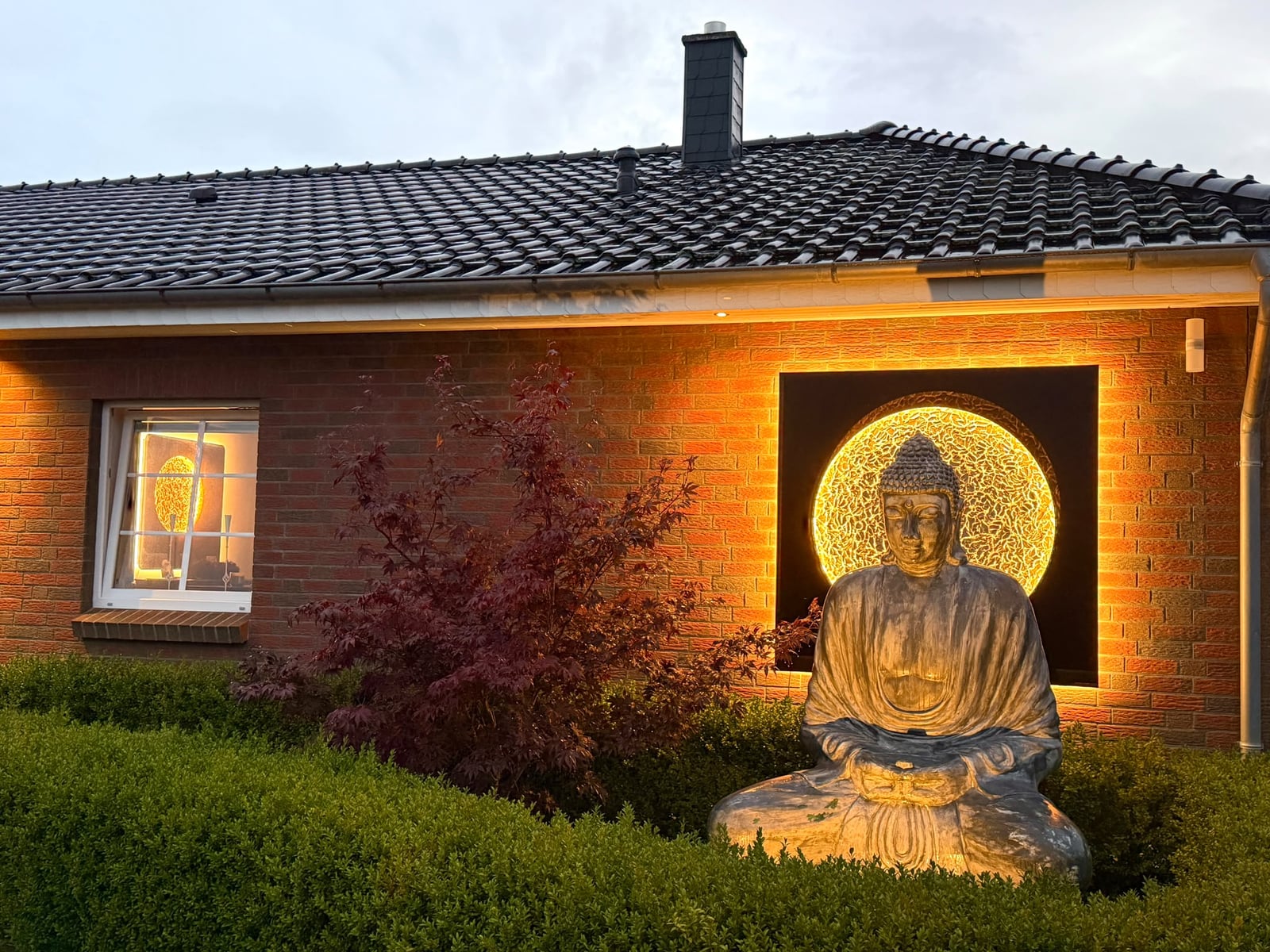 Sonnenmond in Klavierlack Schwarz Dezente Strahlen mit Mond Bronze Deluxe, 160 x 160 cm, beleuchtet, an einer Klinkerfassade